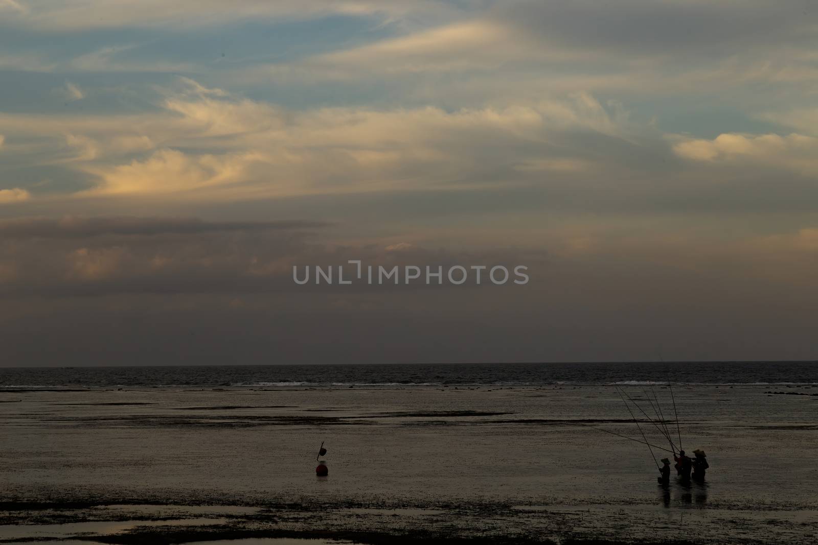 Bali, Indonesia - CIRCA 2018: Group of fisherman fishing for fish in ocean water during sun set with a beautiful colored cloudy sky.