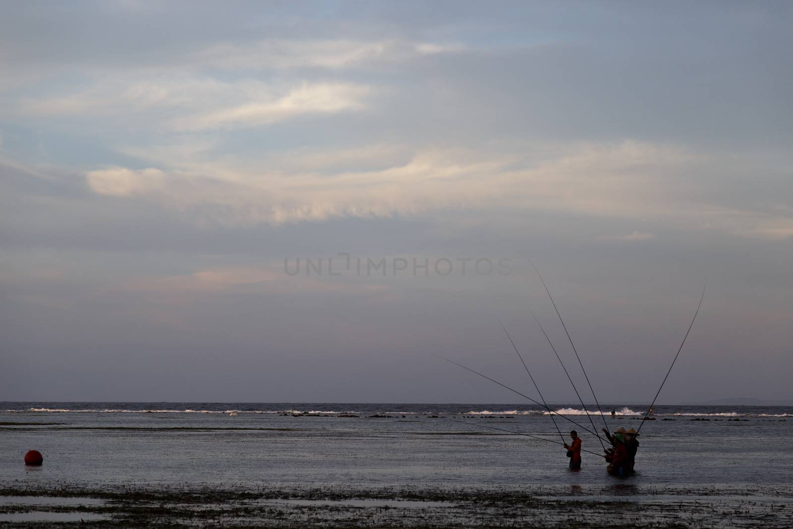 Bali, Indonesia - CIRCA 2018: Group of fisherman fishing for fish in ocean water during sun set with a beautiful colored cloudy sky. by dugulan