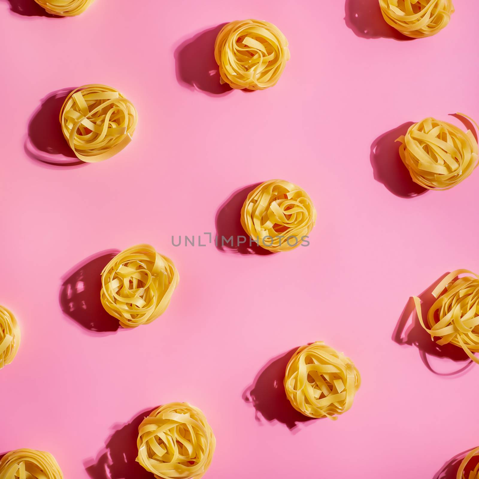 Pasta art. Tagliatelle on pink background in hard light. Creative layout with pasta noodles, top view or flat lay. Square crop. Creative design for menu of italian cuisine with copy space