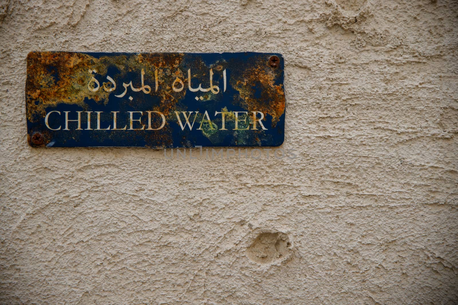 Old chilled water sign with rust on it. Arabic writing can read "Chilled Water" on a rusting blue sign on a traditional arabic house.