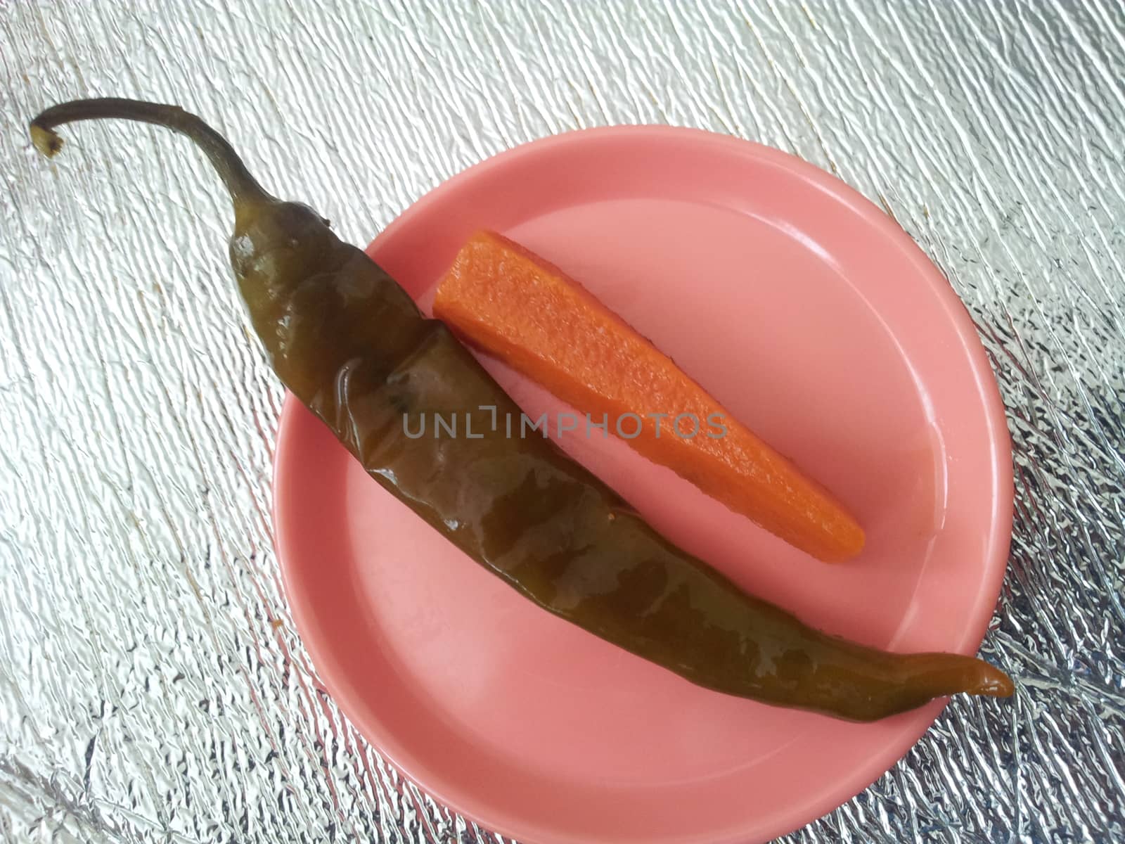 A close up view Green chili pepper with carrot  served in a small plate by Photochowk