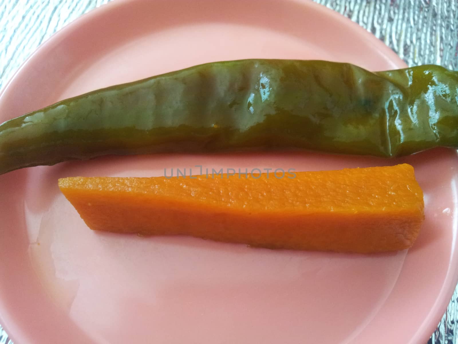 A close up view Green chili pepper with carrot  served in a small plate by Photochowk