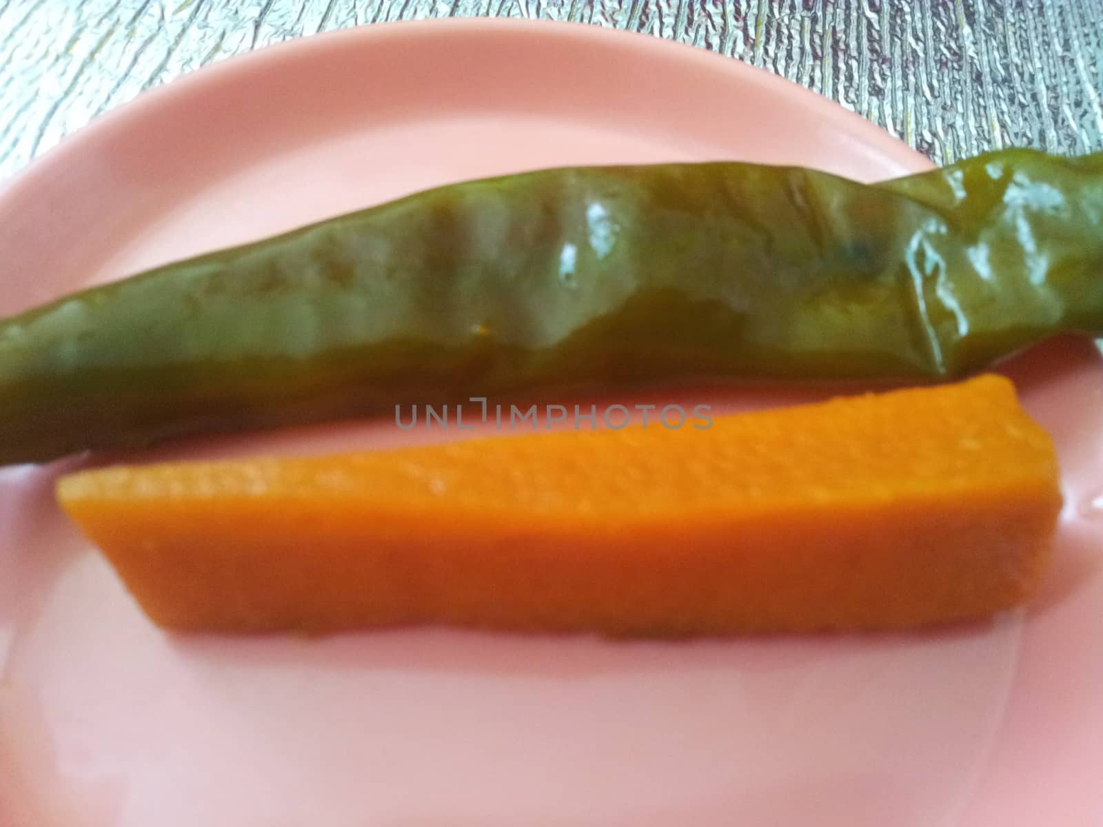 A close up view Green chili pepper with carrot  served in a small plate by Photochowk