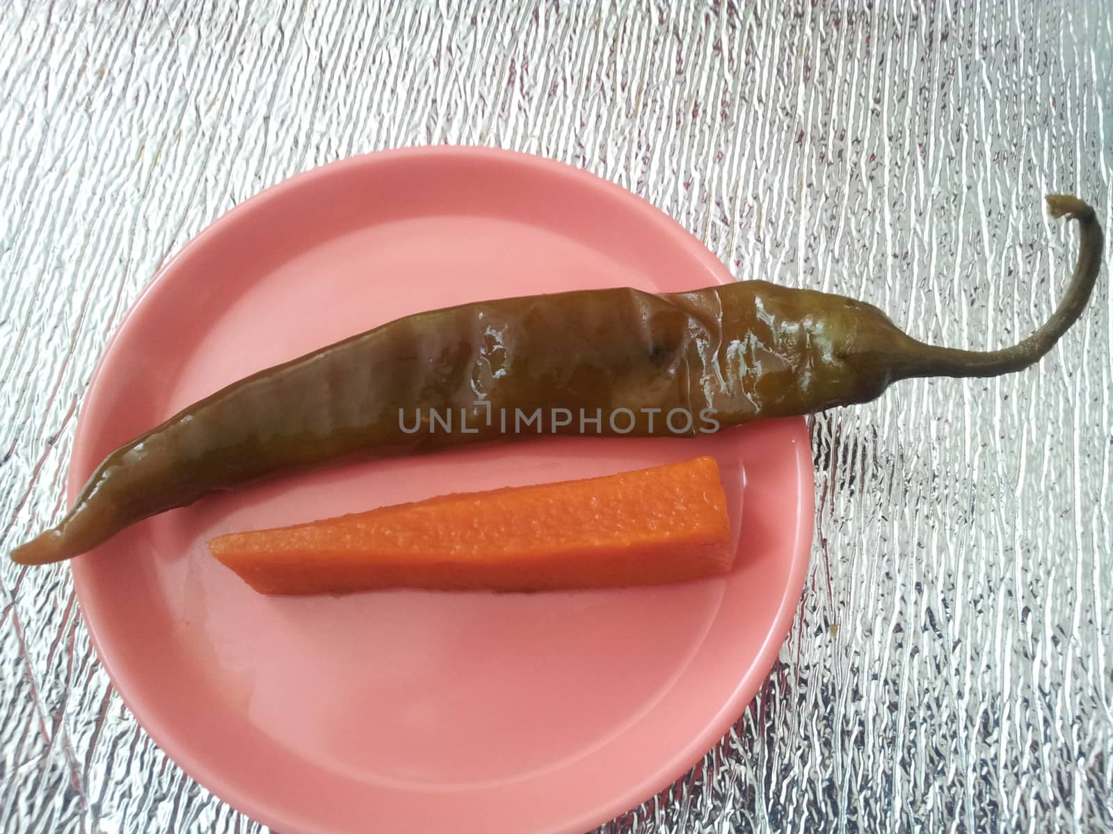 A close up view Green chili pepper with carrot  served in a small plate by Photochowk