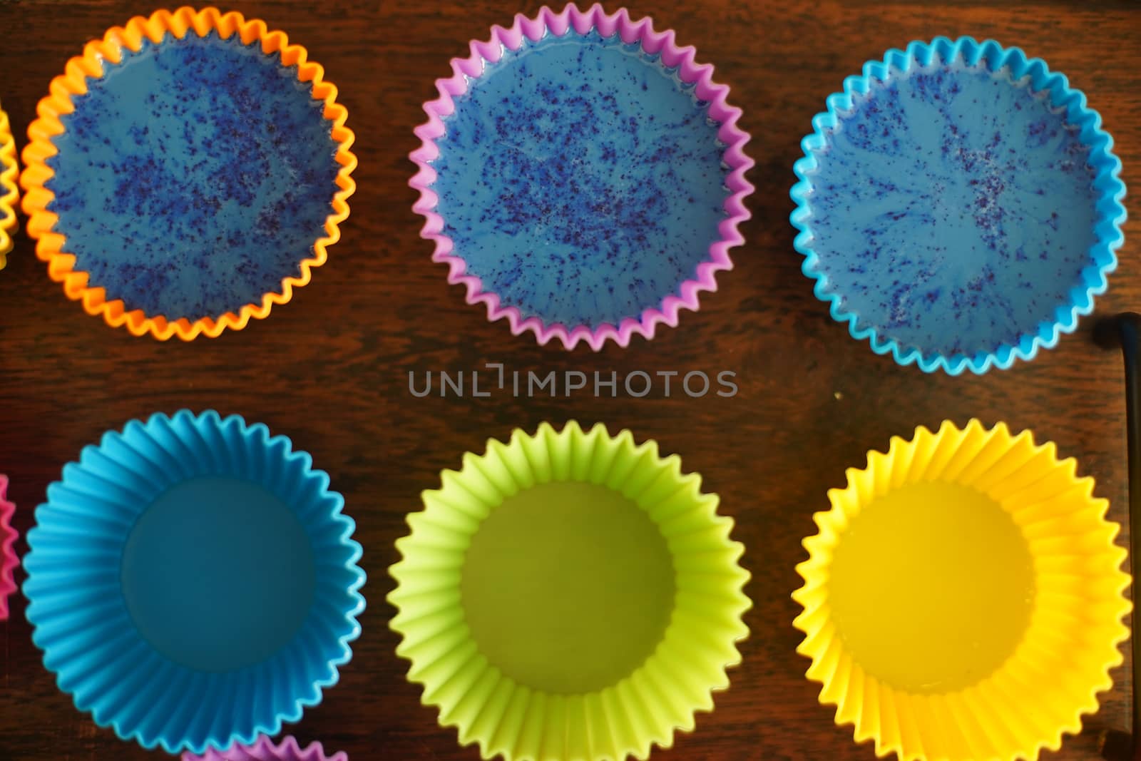 Colorful silicon cupcake molds on wooden coard filled with liquid soap for a home made hobby of melt and pour soapmaking. Shows the beautiful blue glossy liquid used to bake and make cupcakes or muffins.