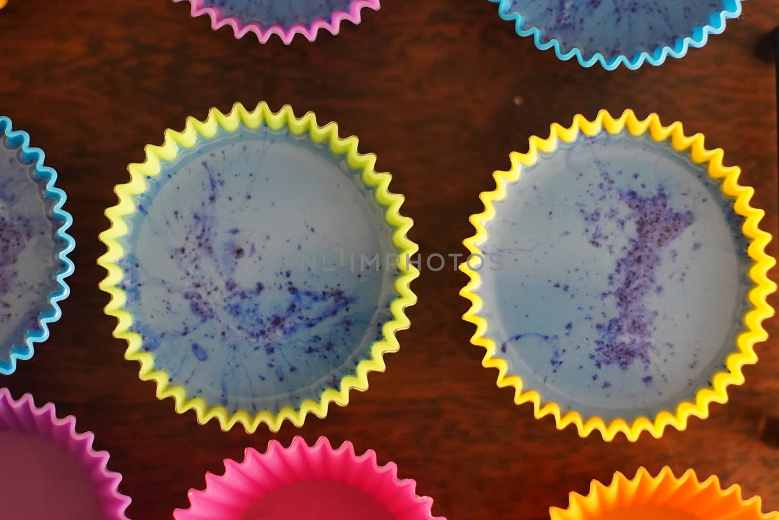 Colorful silicon cupcake molds on wooden coard filled with liquid soap for a home made hobby of melt and pour soapmaking. Shows the beautiful blue glossy liquid used to bake and make cupcakes or muffins.