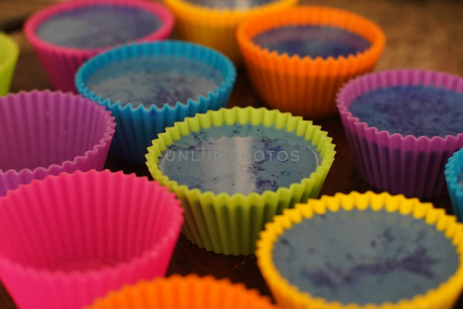 Colorful silicon cupcake molds on wooden coard filled with liquid soap for a home made hobby of melt and pour soapmaking by Shalinimathur