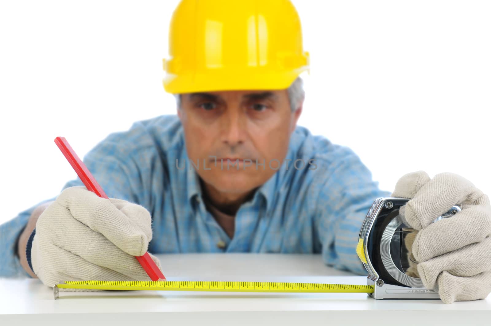Closeup of a construction worker in hard hat using a measuring tape to mark cut line on a board. Focus is on the mans hands and tape measure.