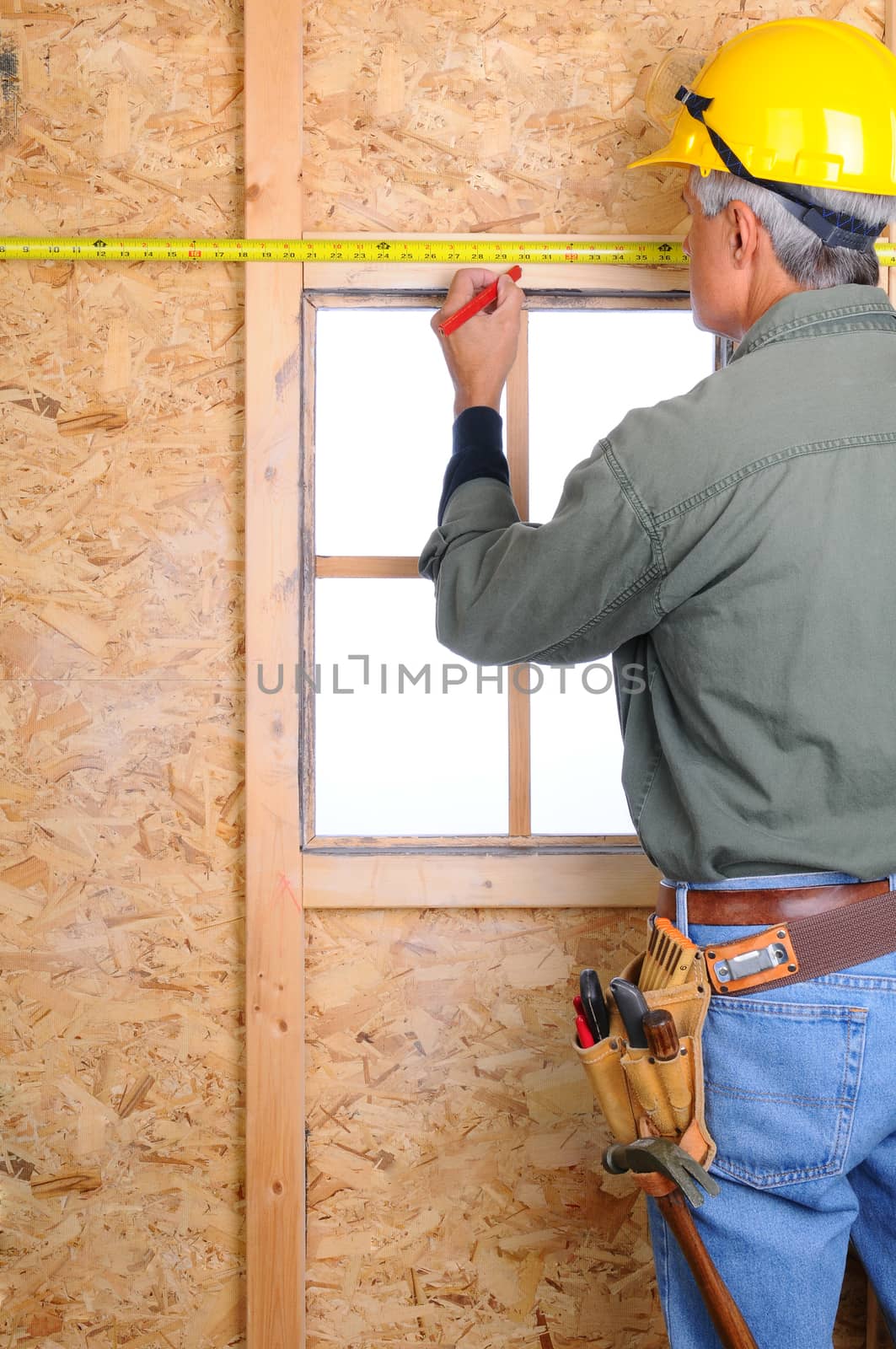 Closeup of a construction worker with a measuring tape marking a point on the wall he is building.