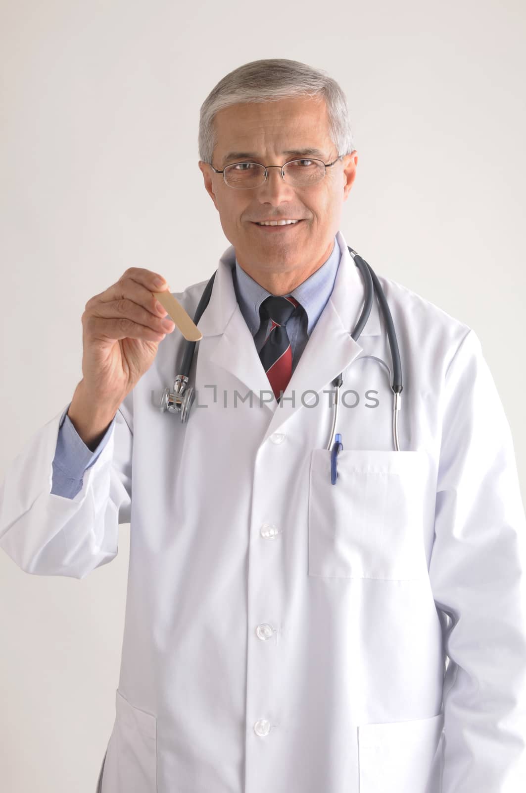 Middle Aged Doctor in Labcoat with Tongue Depressor on gray background vertical format