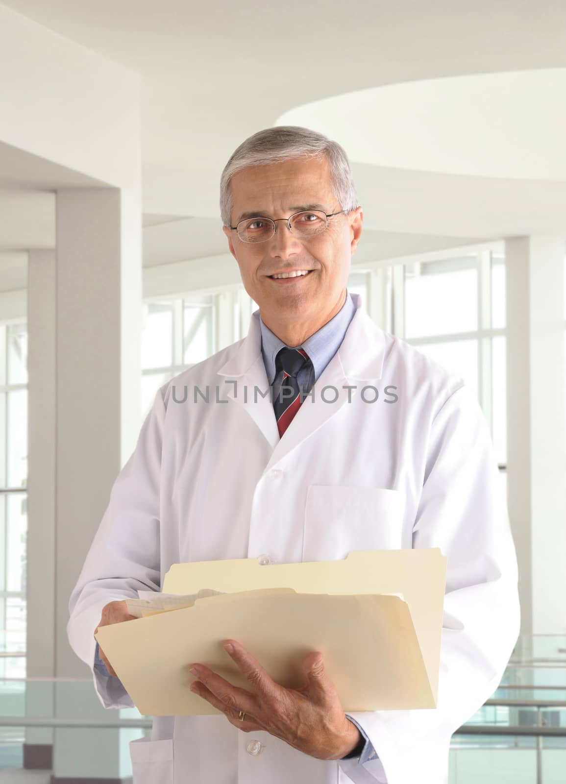 Middle aged male doctor in lab coat holding a manila folder in modern medical office setting. 