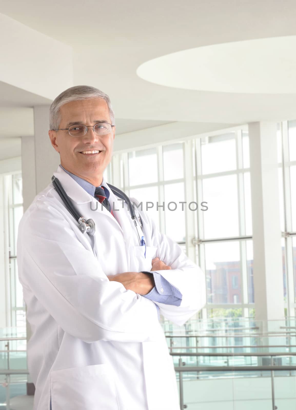 Middle aged doctor wearing lab coat and with arms crossed in modern medical facility