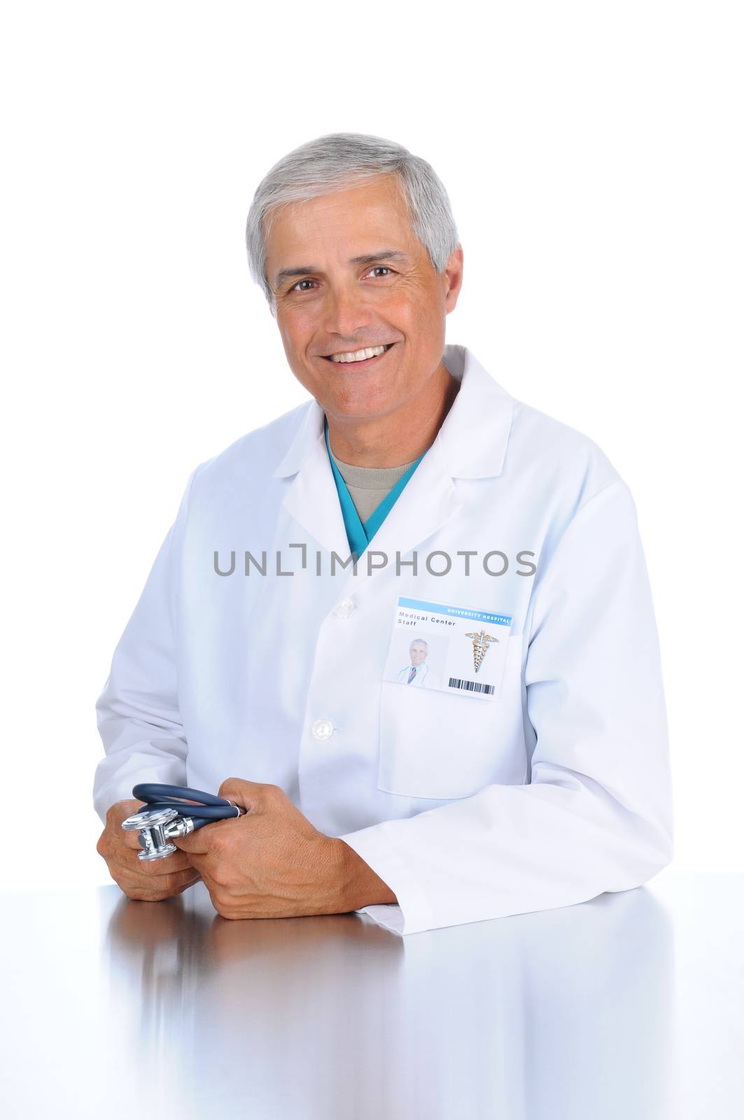 Smiling middle aged doctor seated and holding his stethoscope in both hands. Man is wearing a lab coat and scrubs in vertical format over a white background.