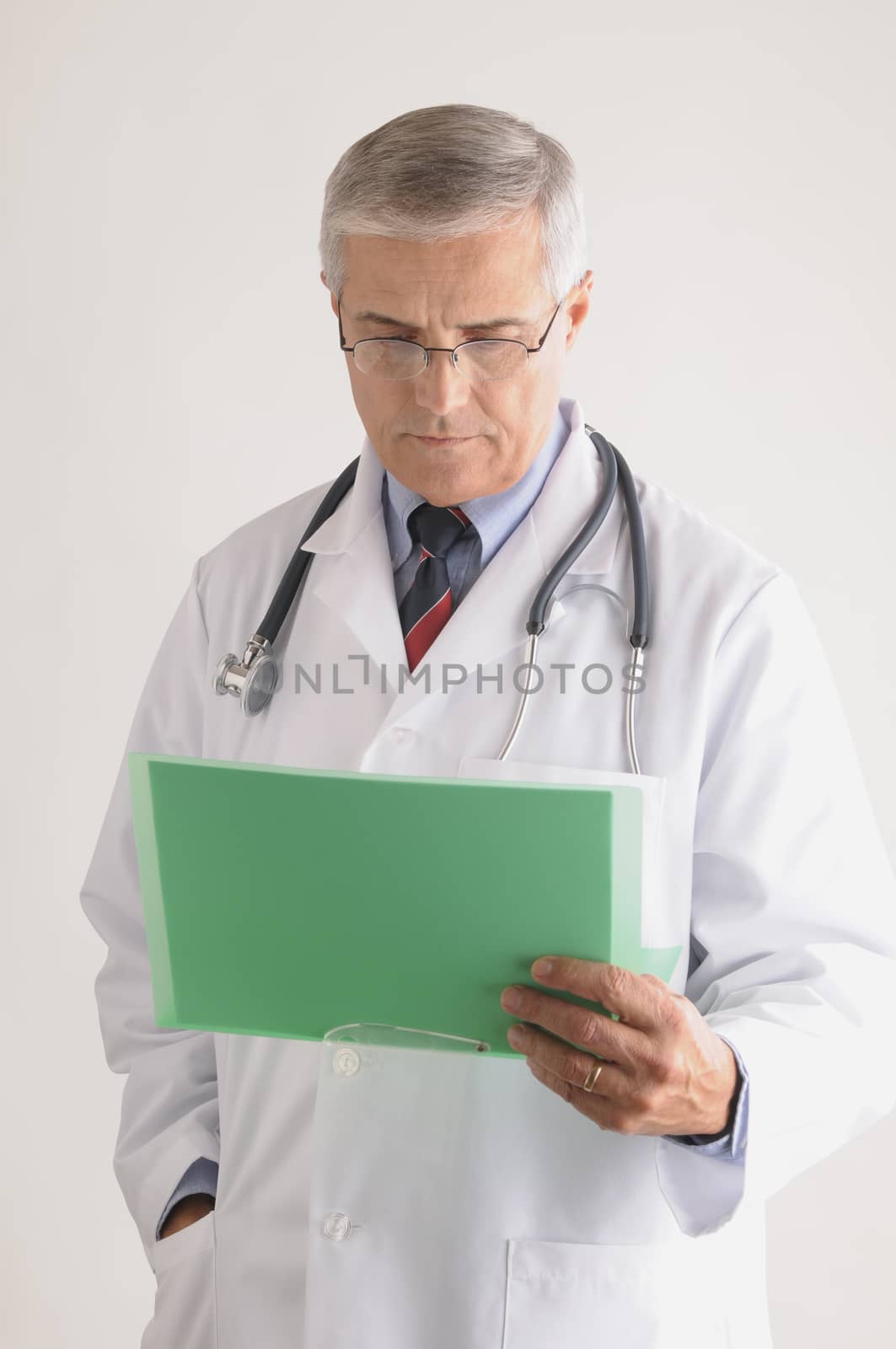 Middle Aged  Doctor in Lab Coat and Stethoscope Looking at a Patients Chart vertical format over gray background