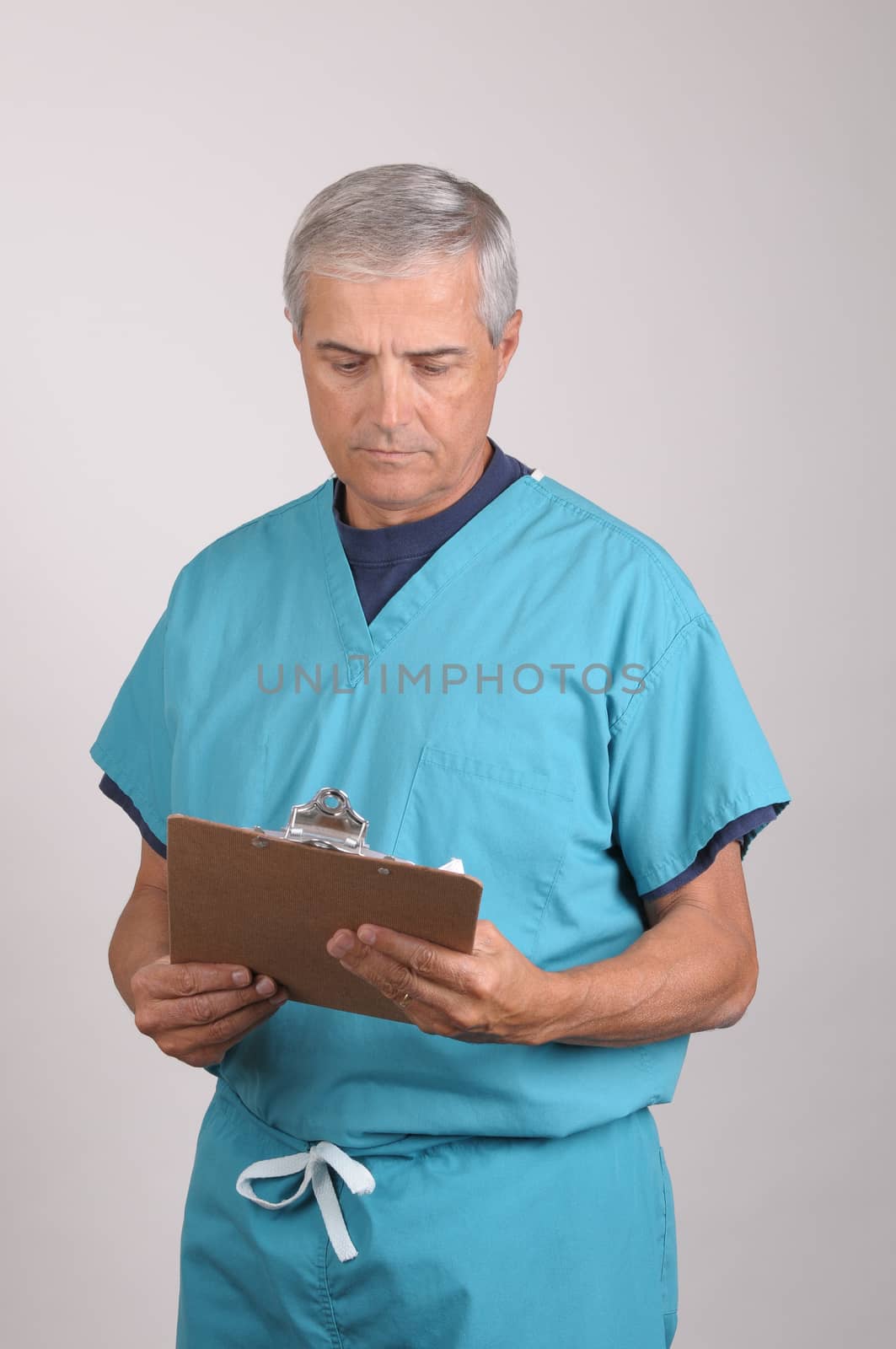 Middle Aged  Doctor in Scrubs Reading a Patients cart on his clipboard