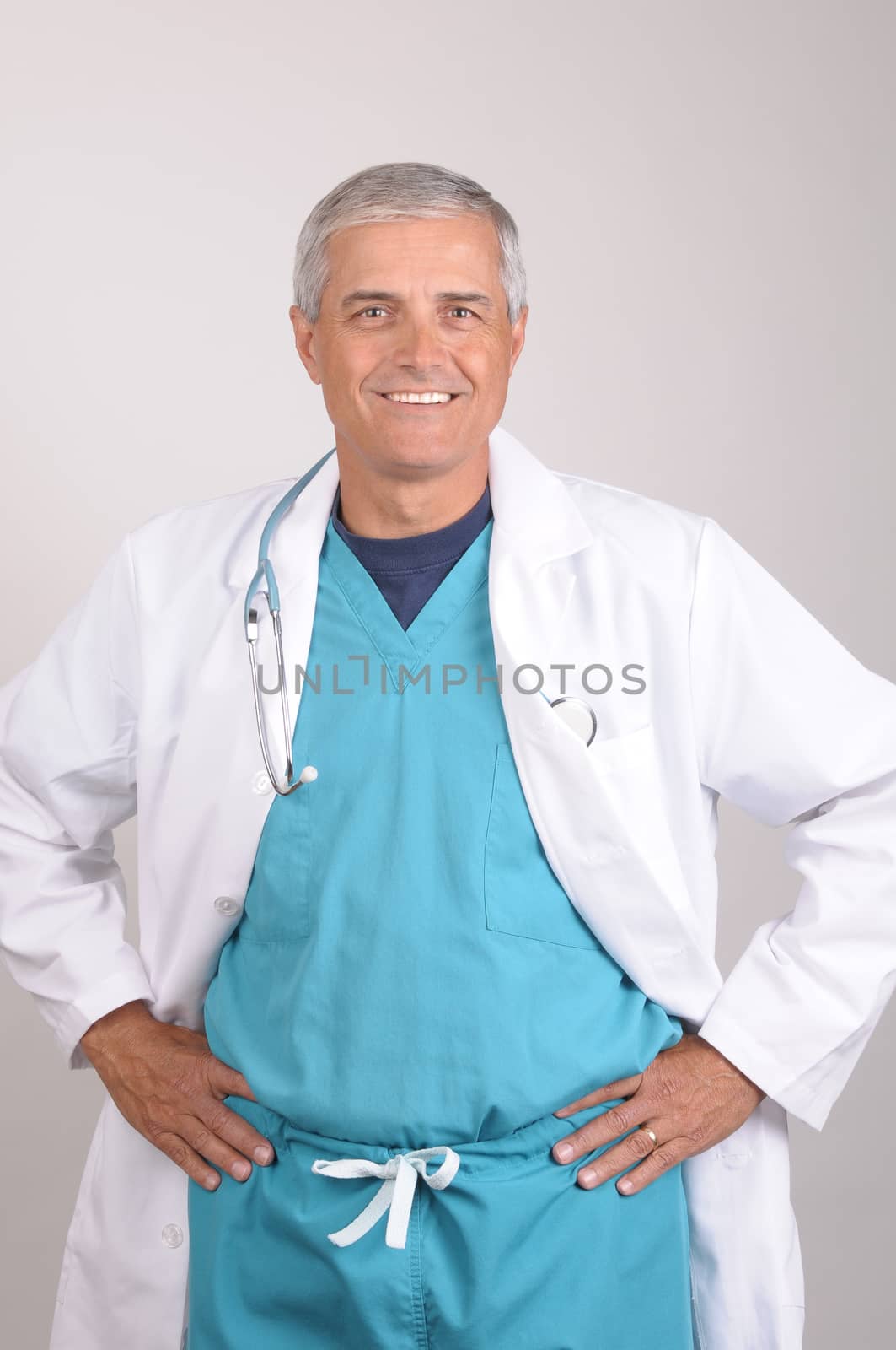 Smiling Middle Aged  Doctor wearing scrubs and lab coat with his hands on his hips