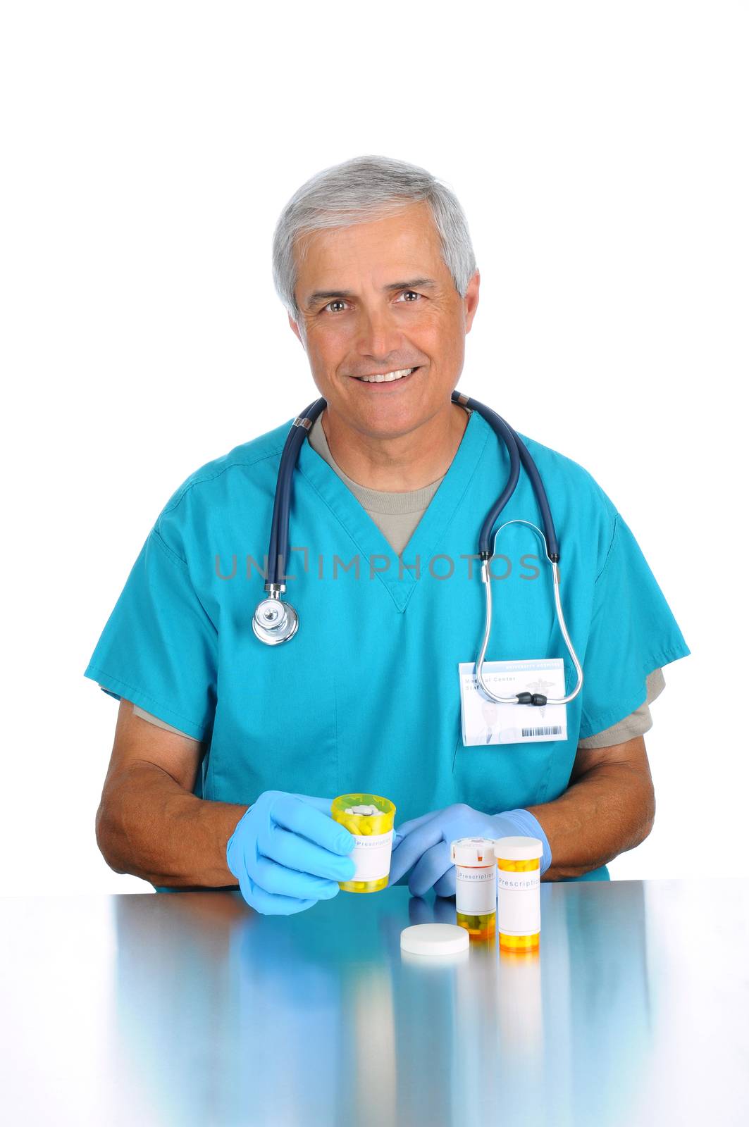 Middle aged doctor wearing scrubs and a stethoscope seated at a counter holding a prescription bottle full of pills. Vertical format isolated on white.