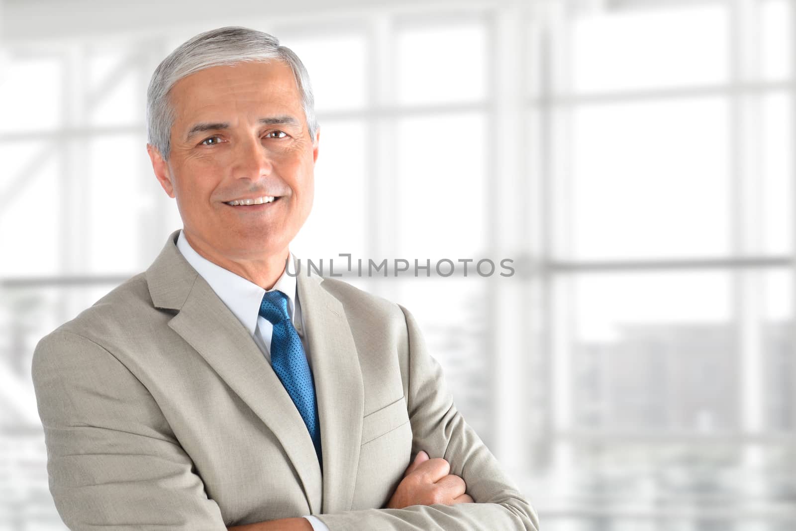 Closeup of a senior businessman with his arms folded in an office interior. Horizontal format with copy space.