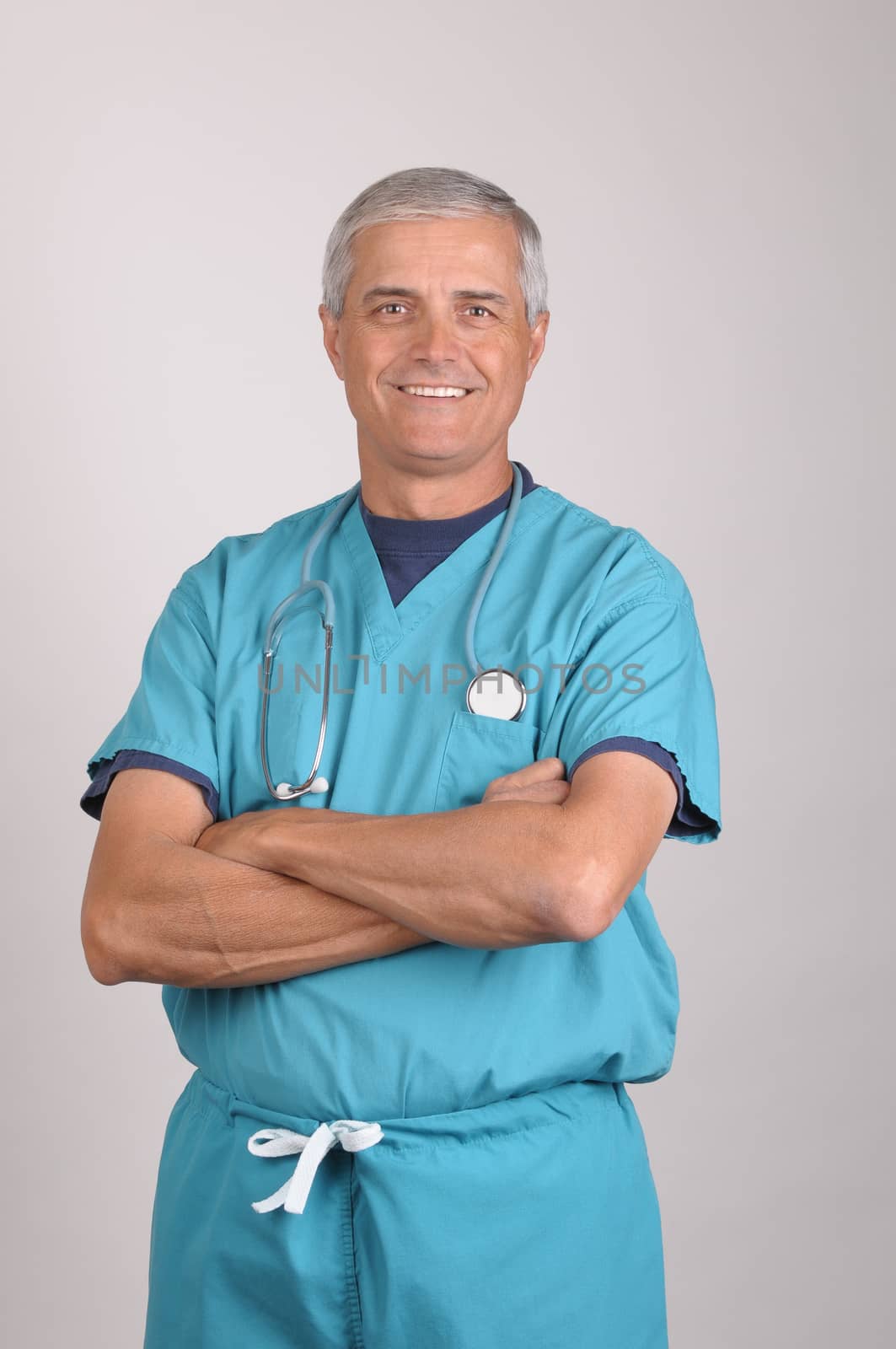Middle Aged  Doctor in Scrubs with his arms folded over gray background vertical composition