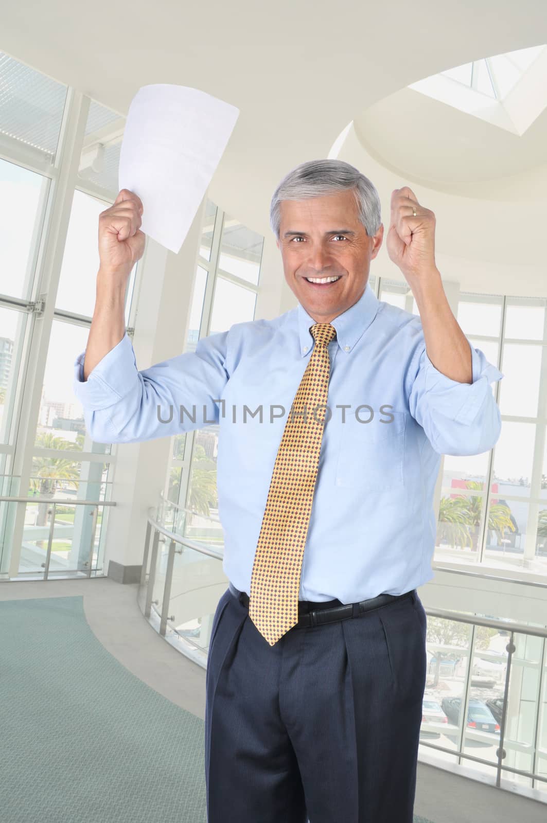 Happy Middle Aged Businessman In Office Holding a Contract in his Hands that are Raised in a victory gesture vertical format