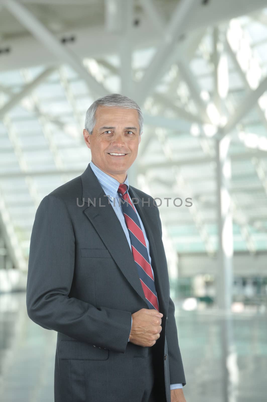 Middle aged businessman standing in modern office lobby. Vertical format with man smiling at the camera.