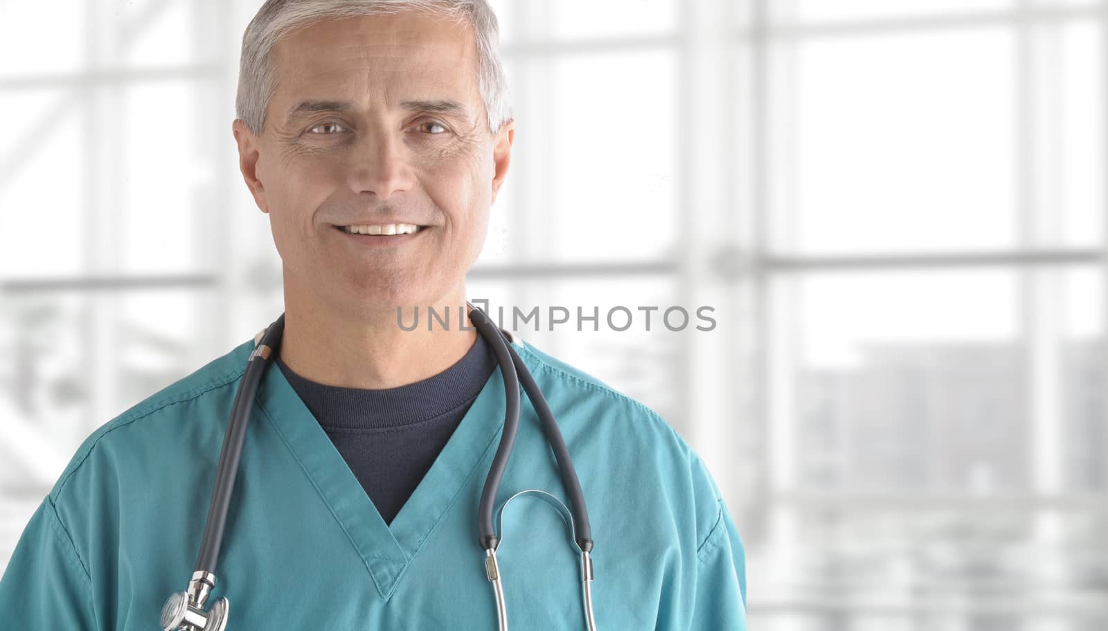 Portrait of smiling senior doctor standing against office window background while looking at camera.