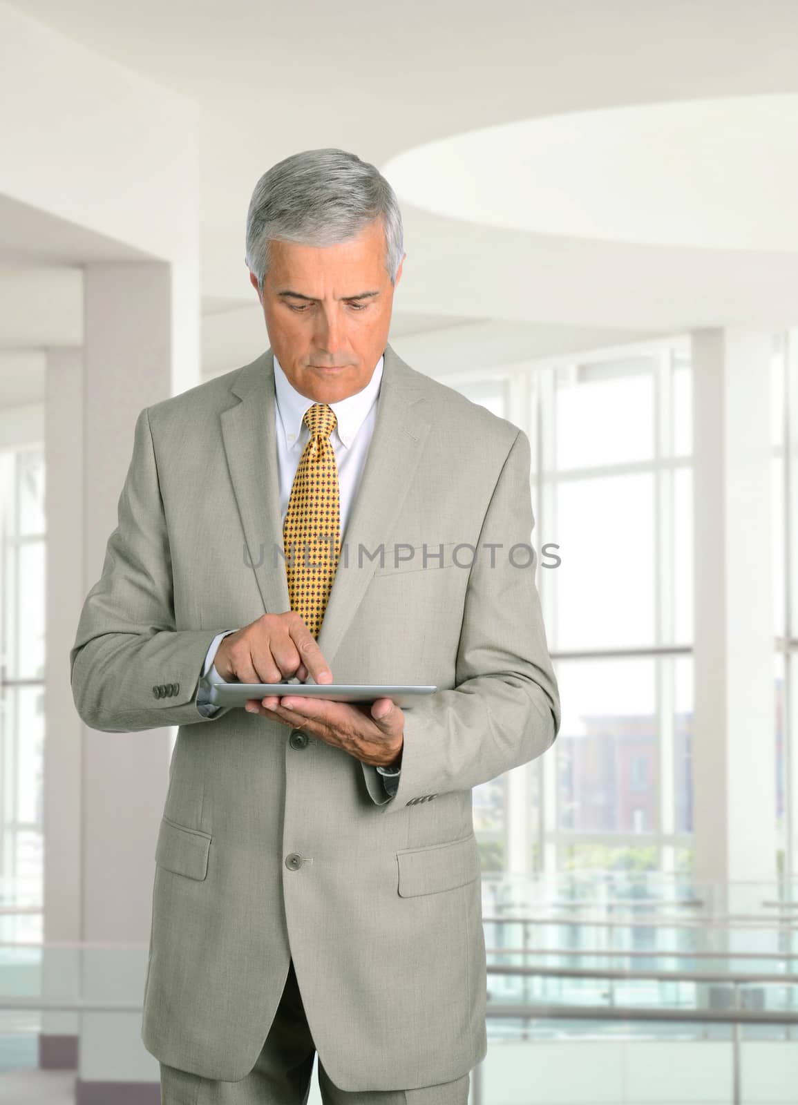 Middle aged businessman looking at his tablet computer while standing in a modern office building.