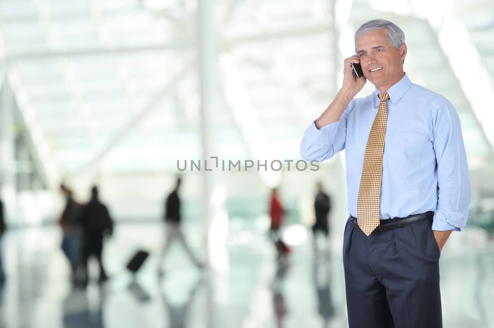 Middle aged Business Traveler Talking on Cell Phone in Airport Concourse with blurred travelers in background