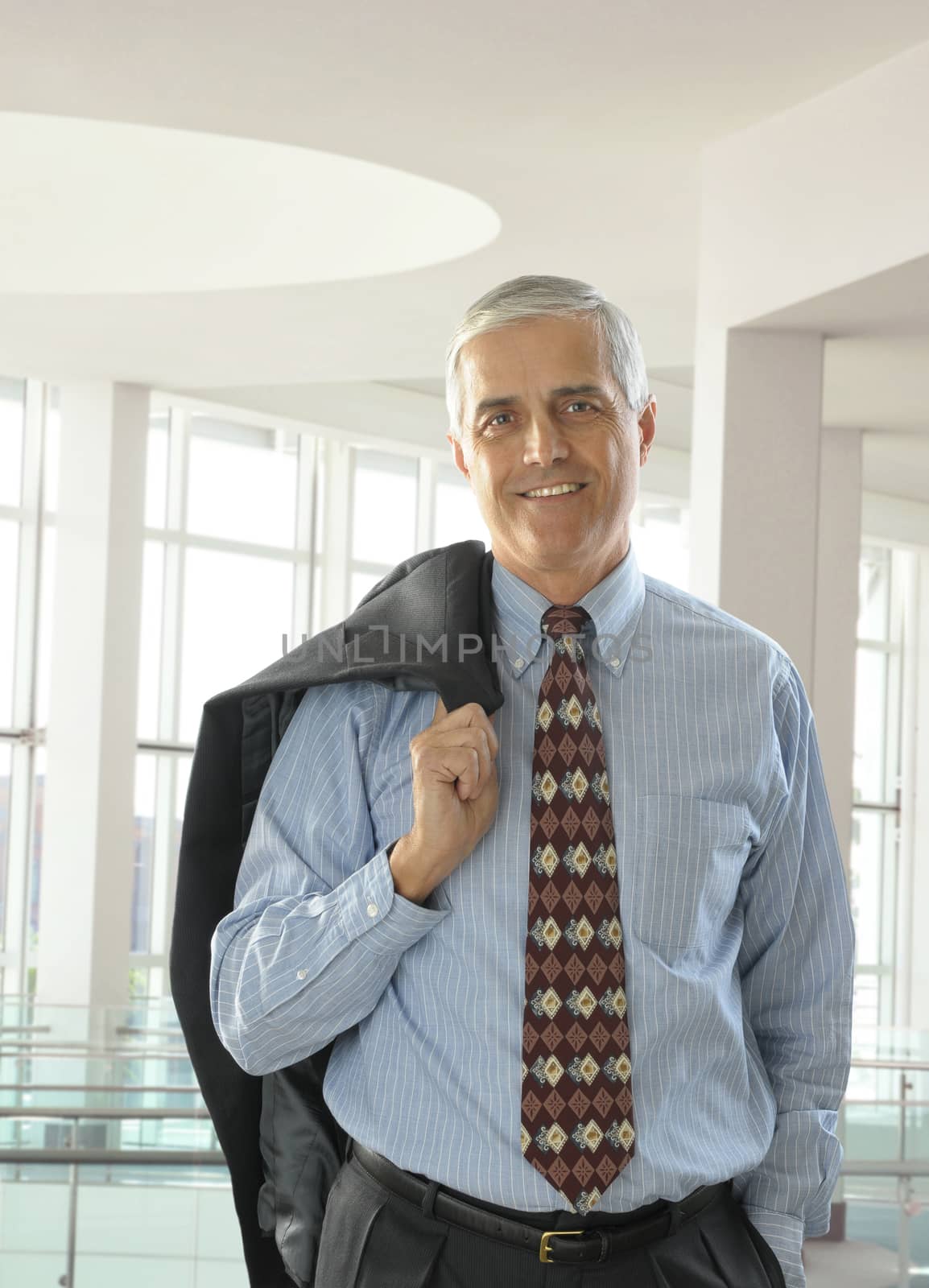 Smiling Middle Aged Businessman Standing in Modern office setting with Jacket over shoulder