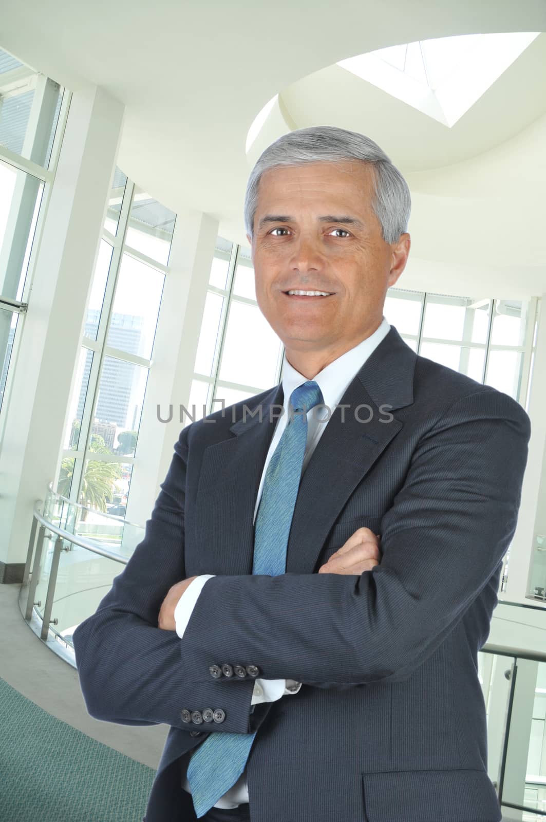 Middle aged Businessman in Lobby of modern Building with His Arms Folded, Vertical Format.