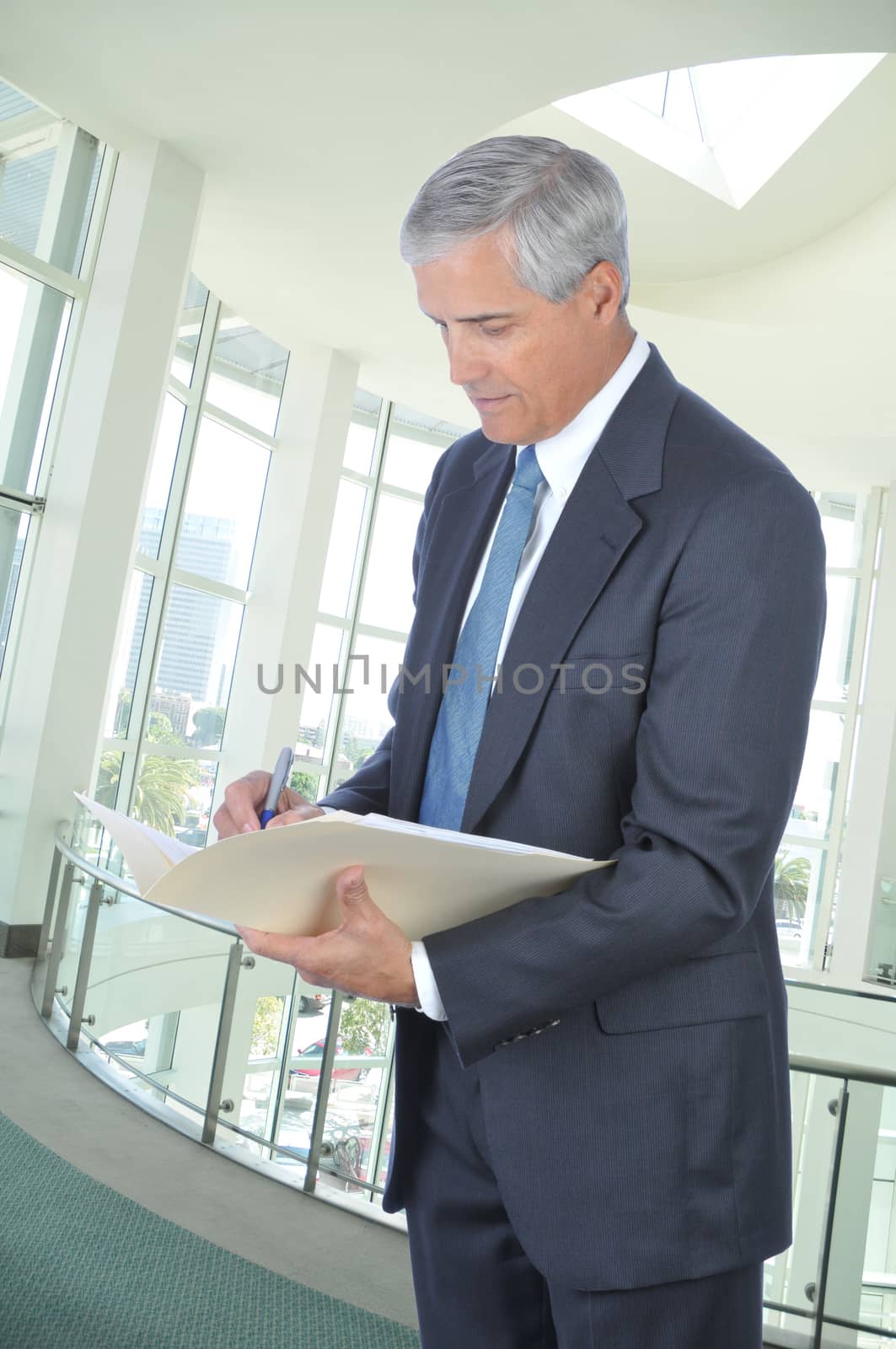 Standing Middle aged Businessman Writing in File Folder in Office Setting
