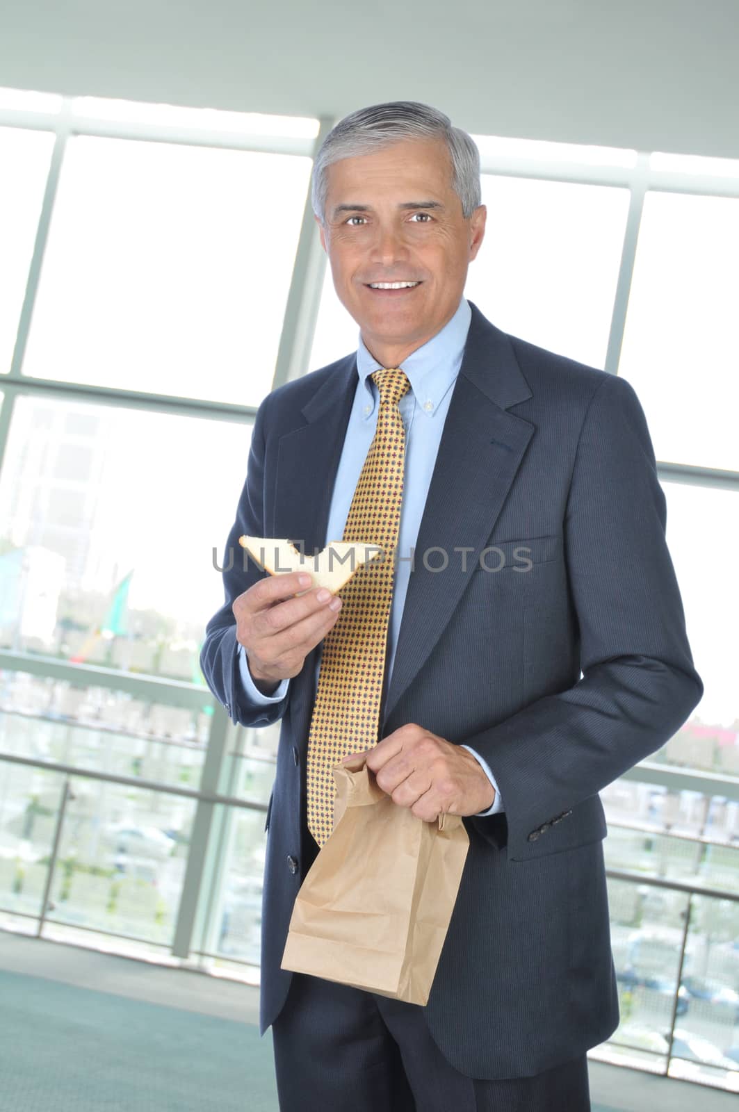 Middle aged Businessman in office building holding brown bag and sandwich