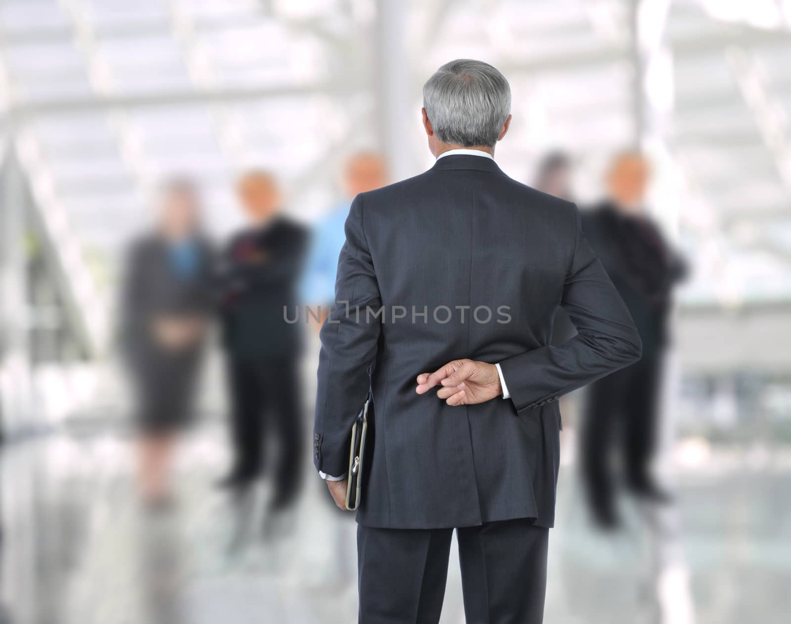 Standing Businessman with fingers crossed behind back. He is standing in front of an out of focus group of people. Horizontal format.