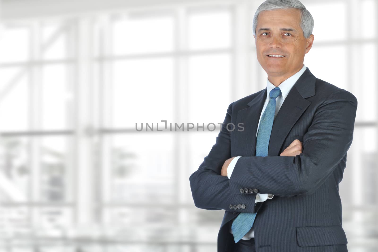 Portrait of smiling senior businessman standing against office window background while looking at camera.