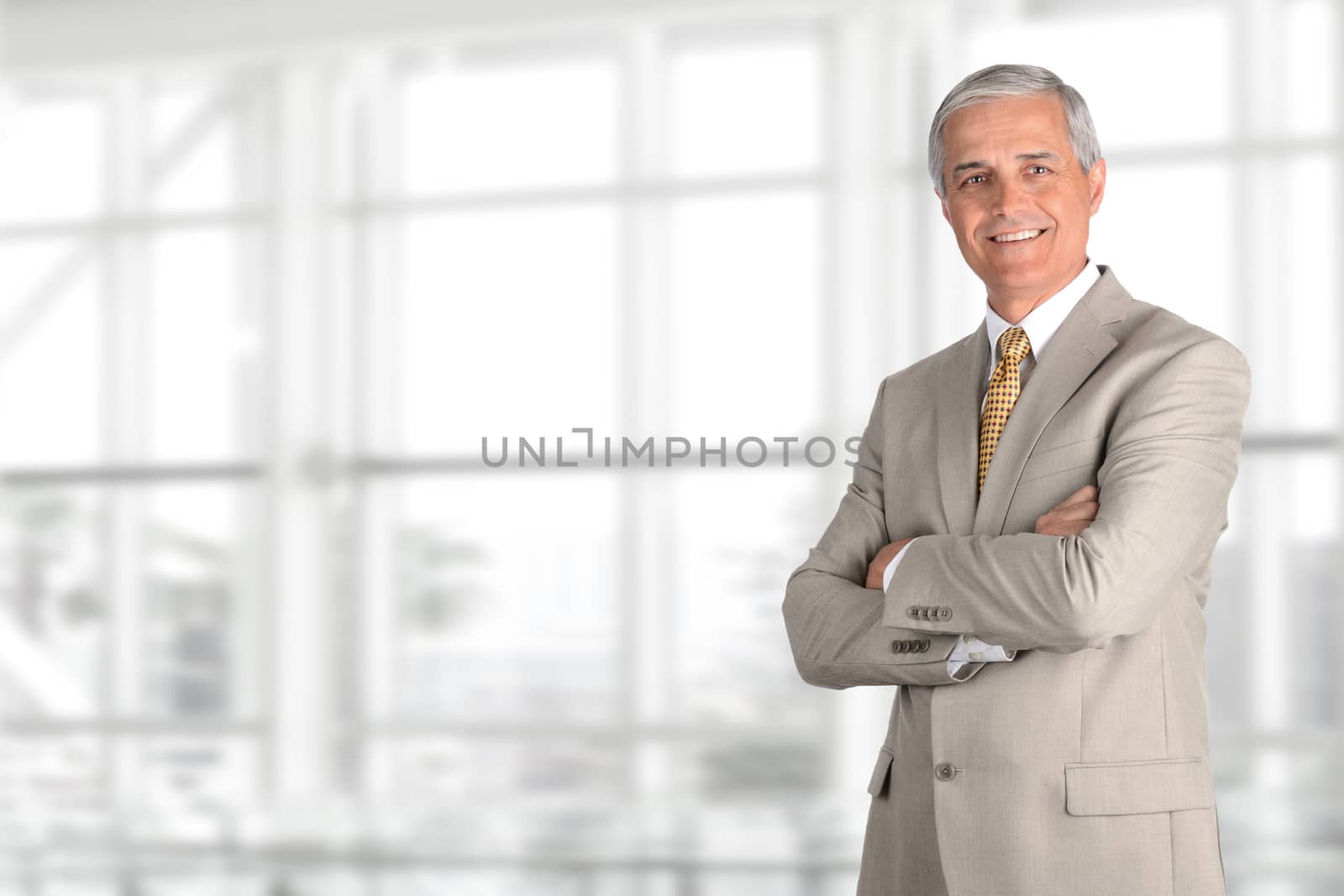 A mature businessman standing with his arms crossed in a modern office building. Horizontal format with copy space.