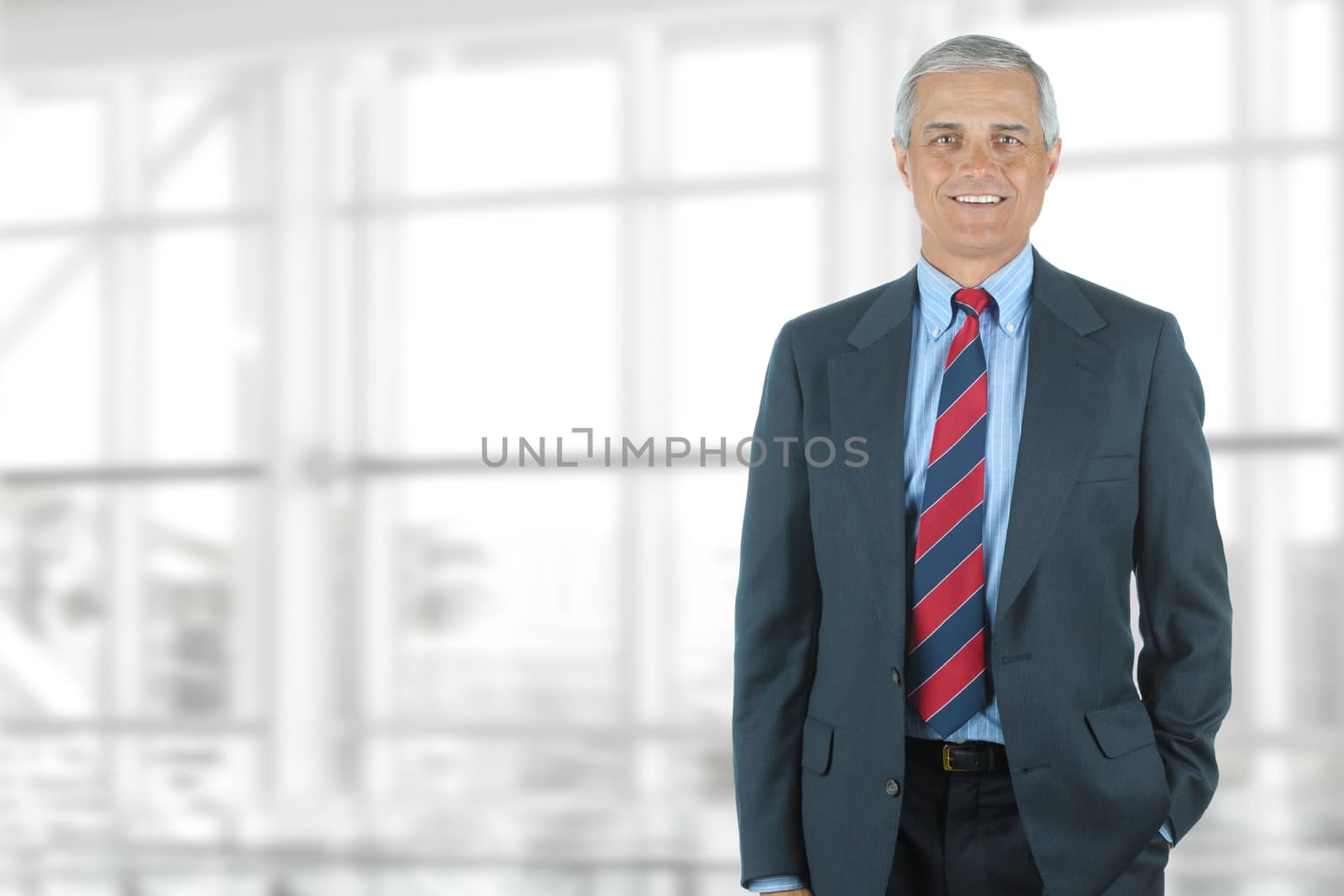 Portrait of smiling senior businessman standing against office window background while looking at camera.
