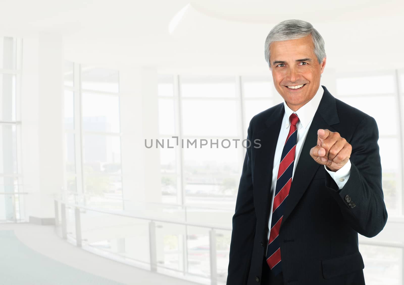 Mature businessman standing in a high key office setting pointing at the camera.