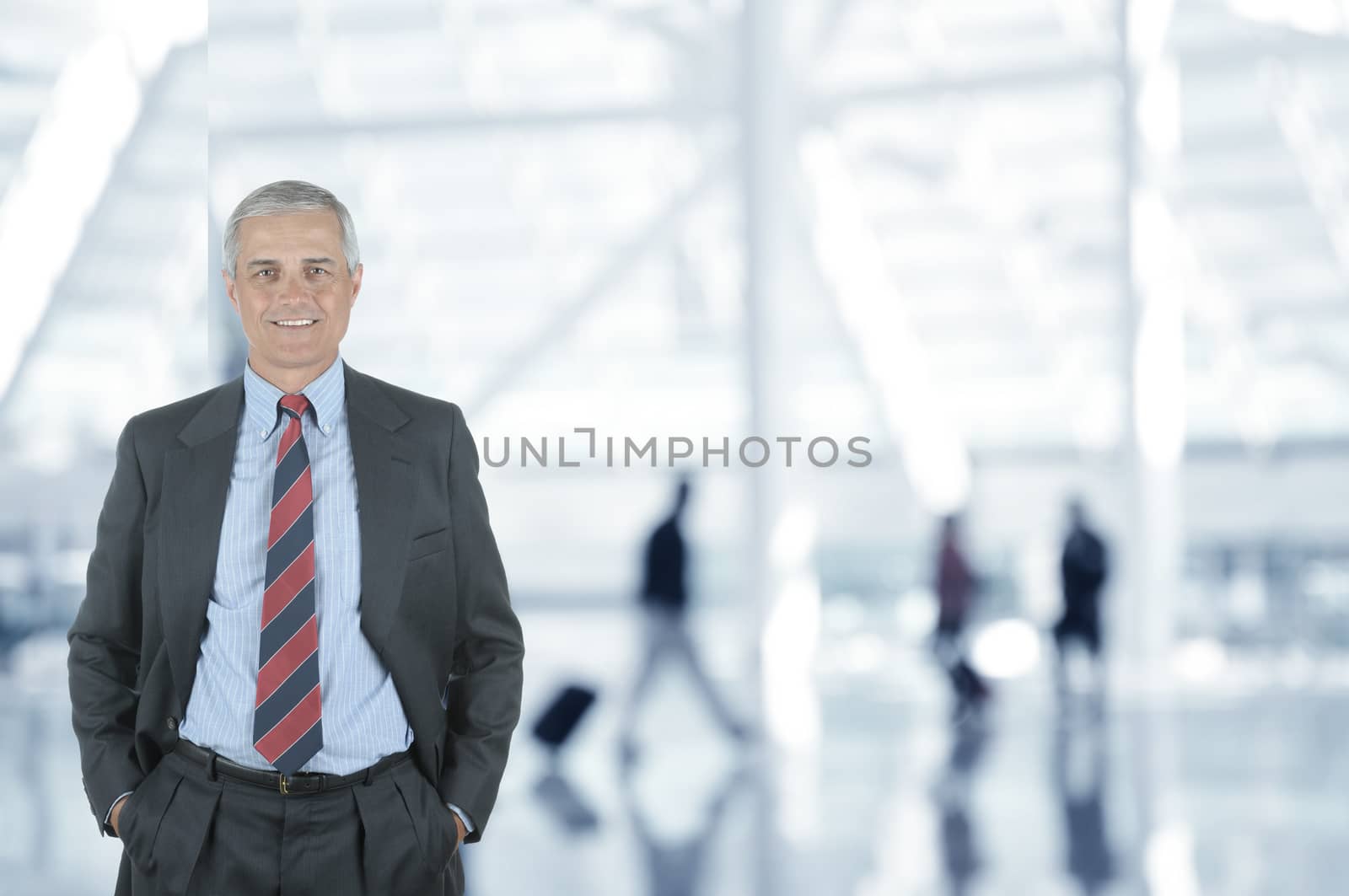 A Businessman in Airport Terminal with his hands in pockets, blurred travelers are in the background