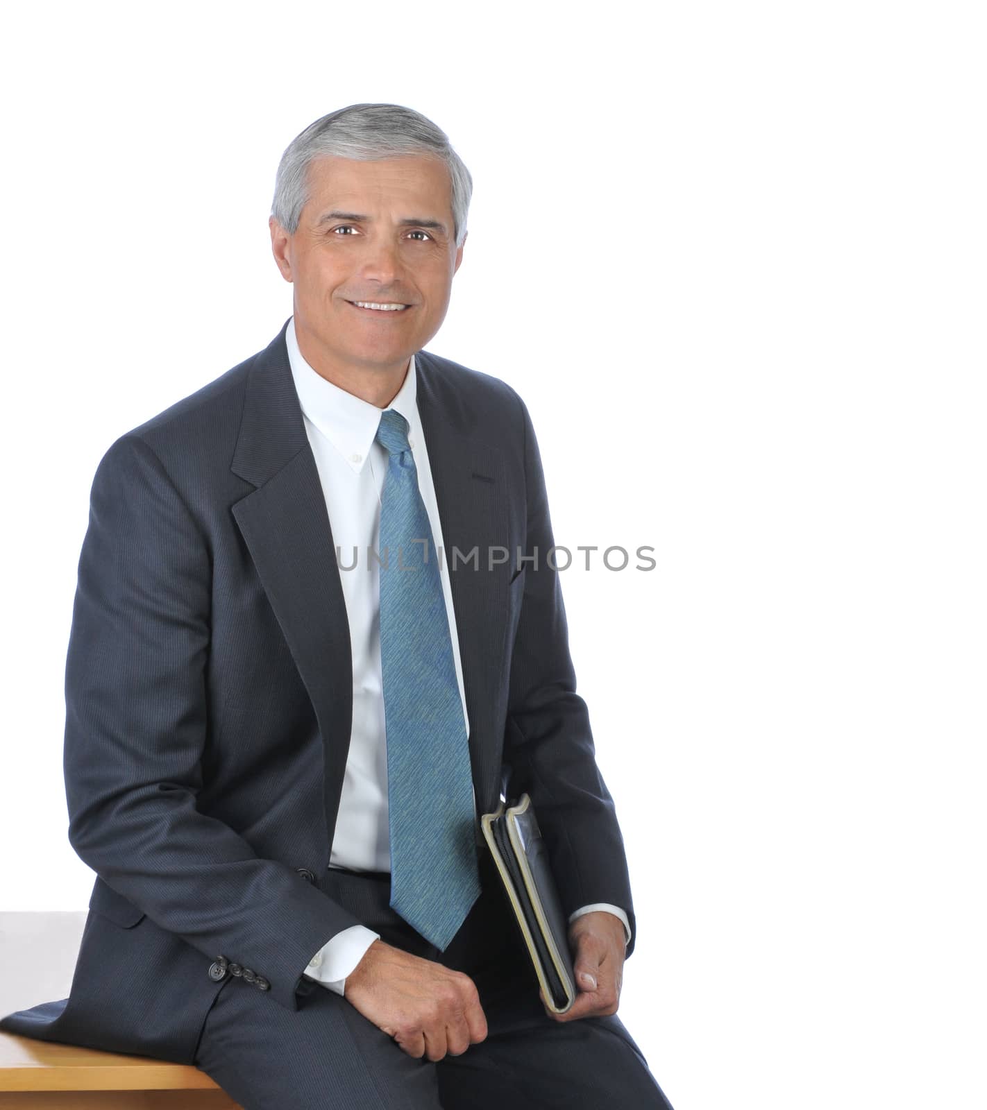 Smiling businessman sitting on the edge of his desk isolated over white