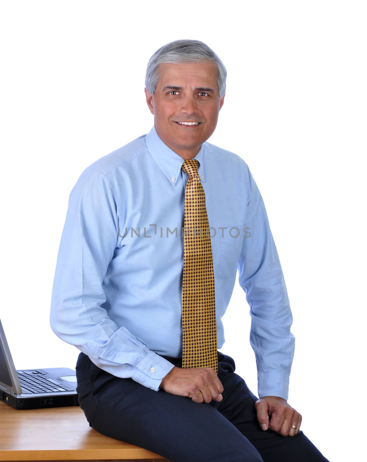 Smiling businessman sitting on the edge of his desk isolated over white