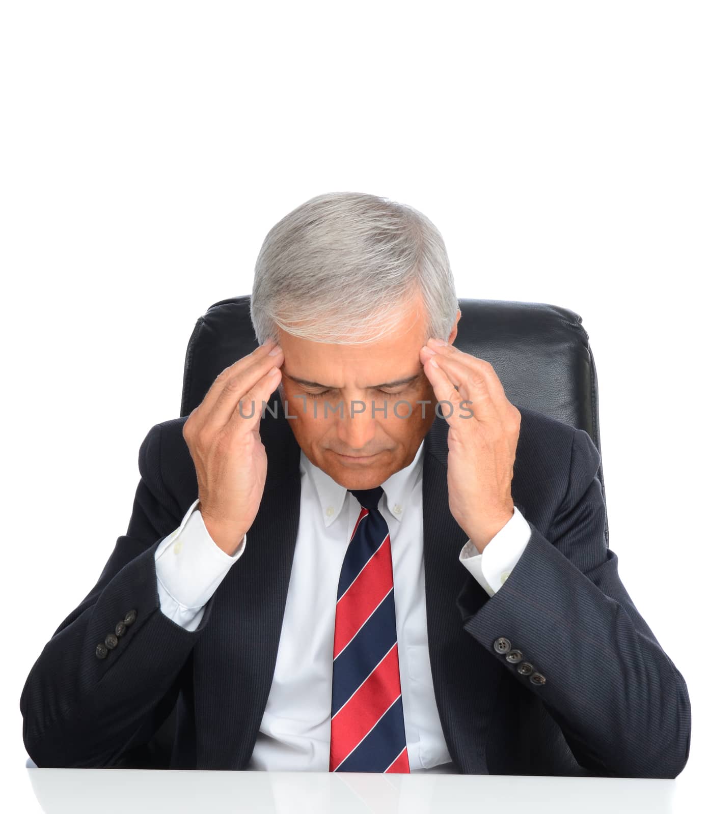 Mature businessman seated at his desk holding his temples to ease a migraine headache. Square format over a white background.
