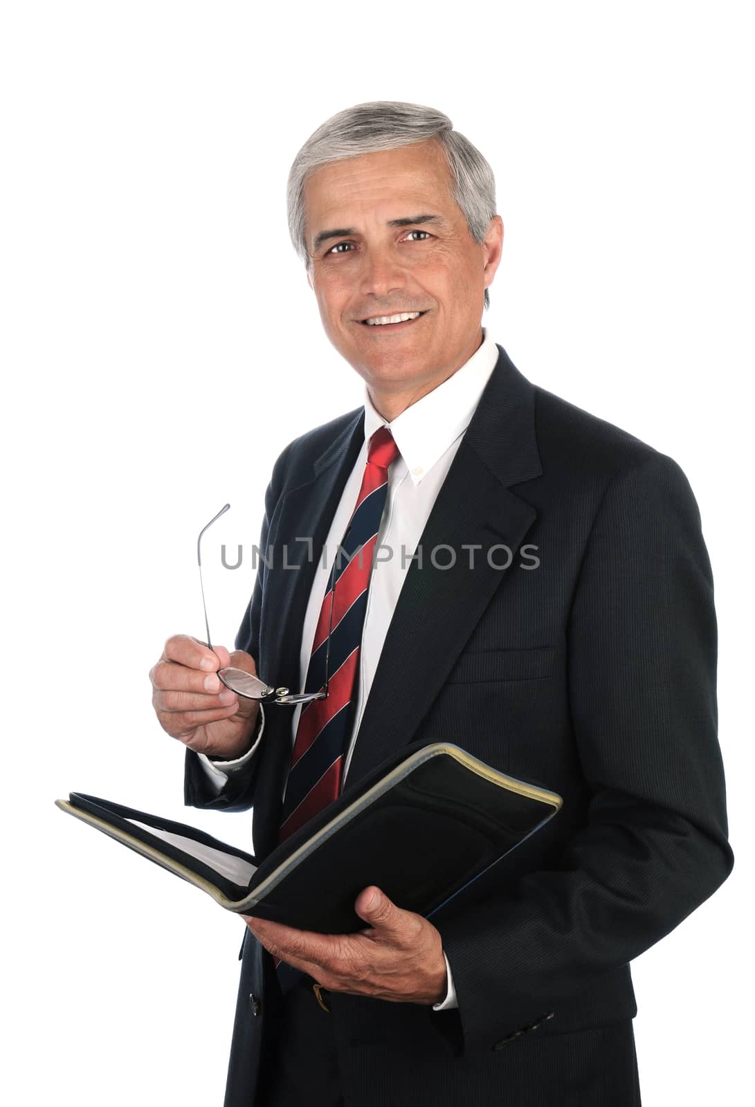 Smiling middle aged businessman holding a binder and his eye glasses while standing isolated on white.