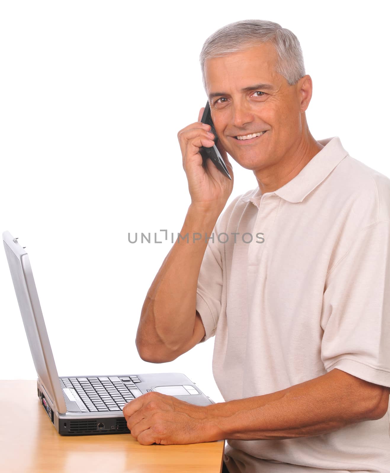 Businessman with Cell Phone Seated at Computer looking towards camera isolated on white