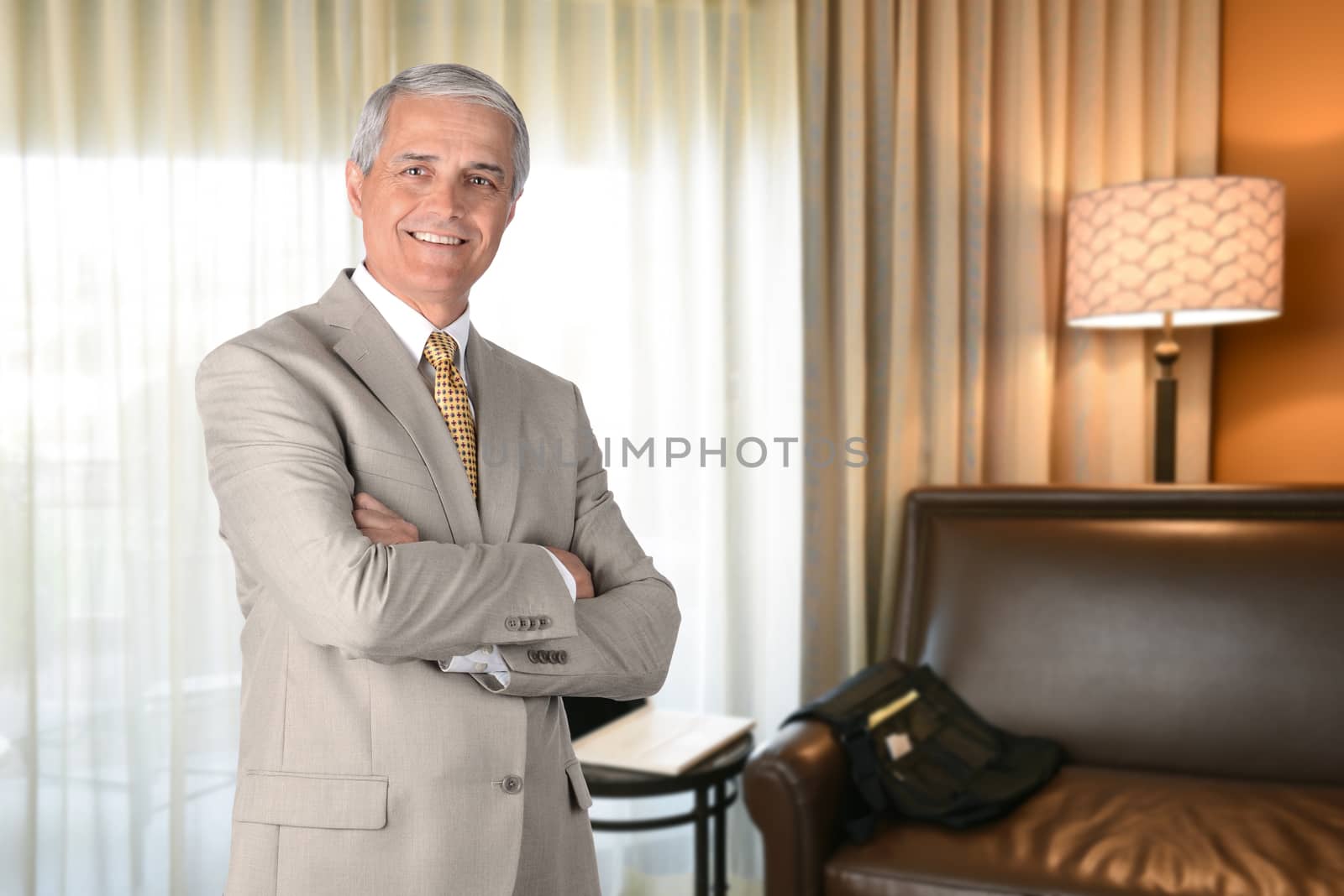 Businessman in hotel room with arms folded and looking at camera. Business travel concept.
