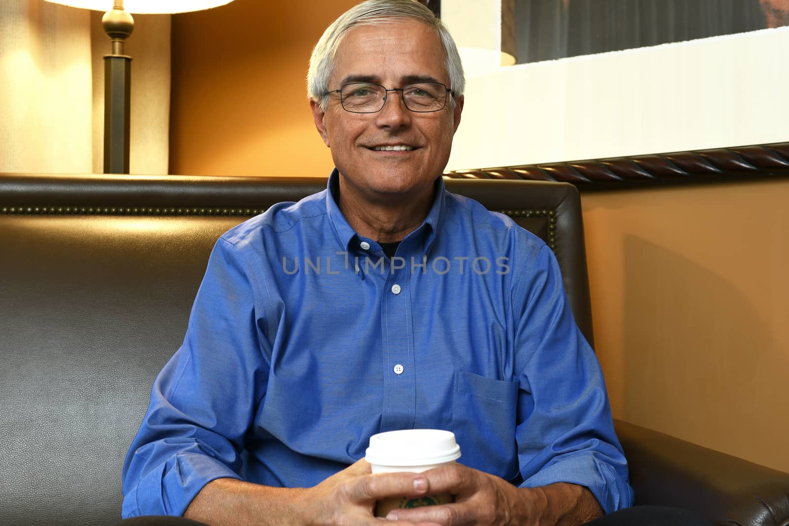 Portrait of a senior businessman seated on the sofa in a hotel room holding a cup of coffee.