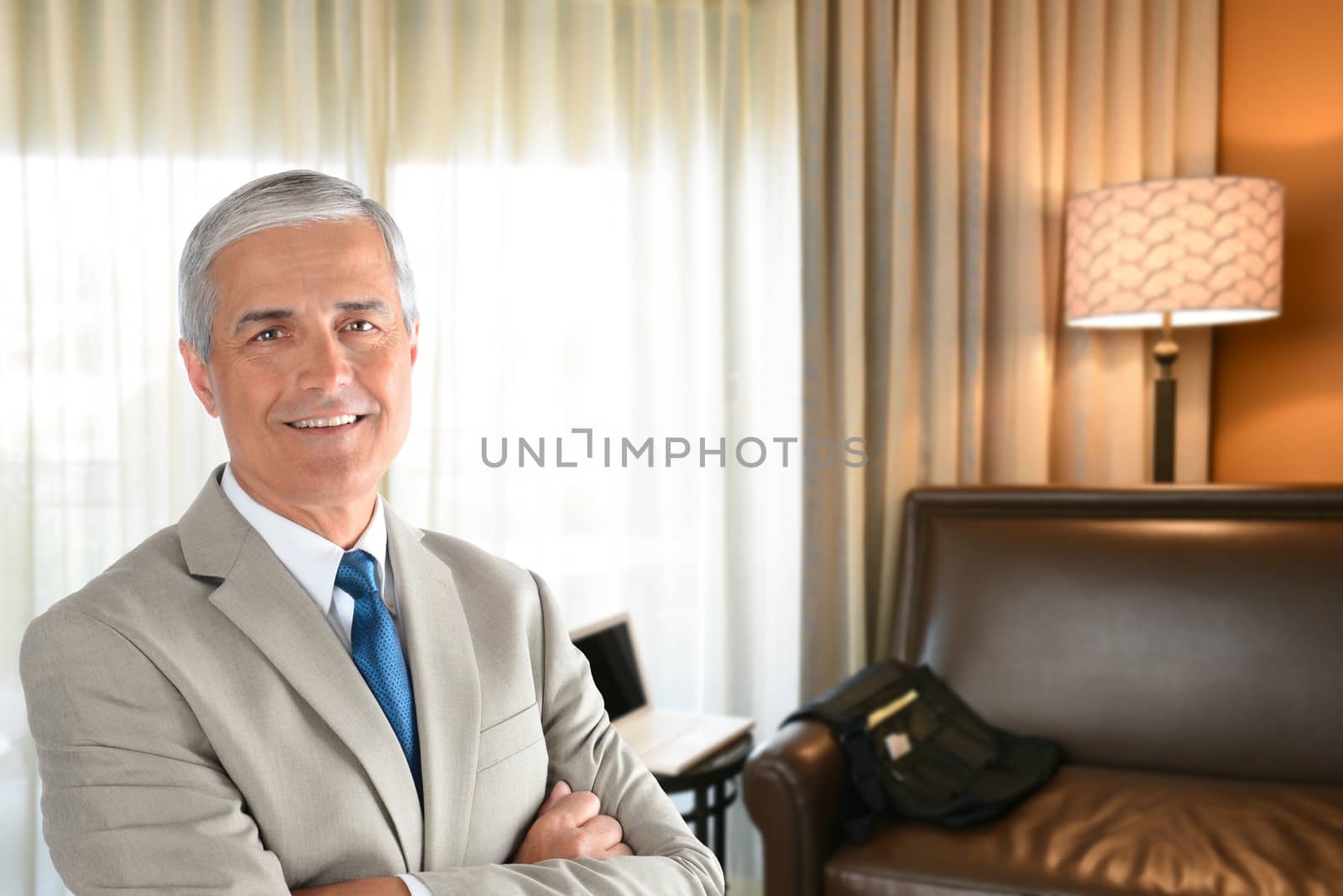 Businessman in hotel room with arms folded and looking at camera.