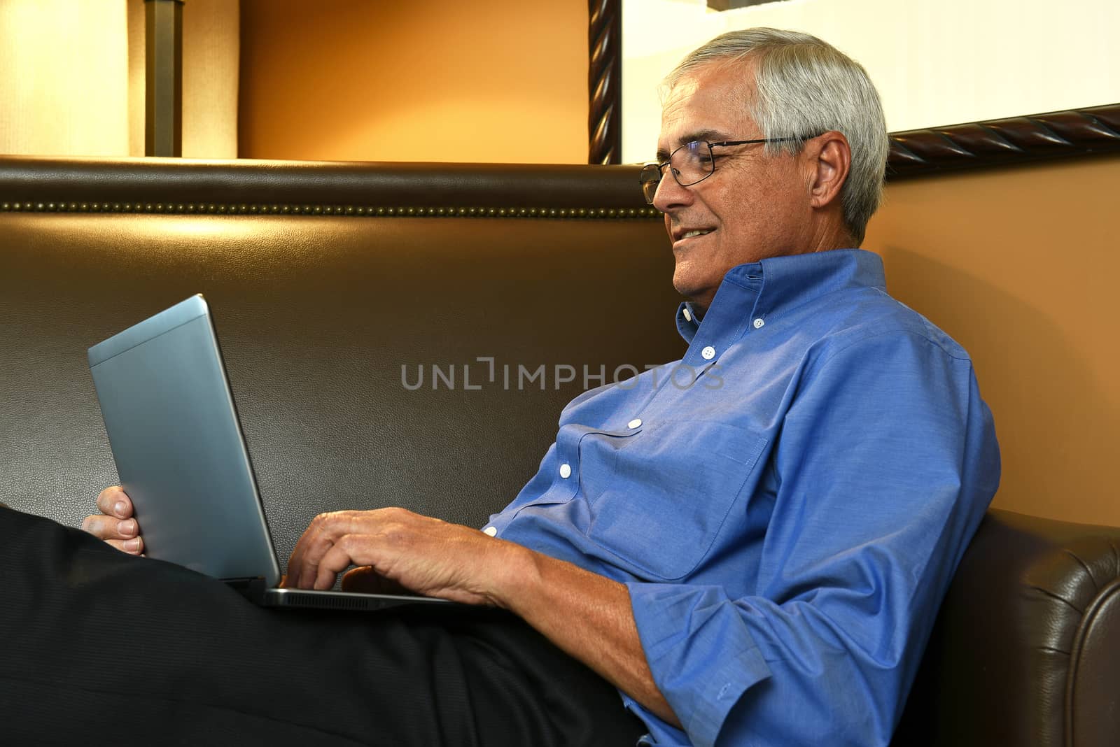 Closeup of a senior businessman sitting on a sofa in his hotel room while using a tablet computer. The man is seen from the side.