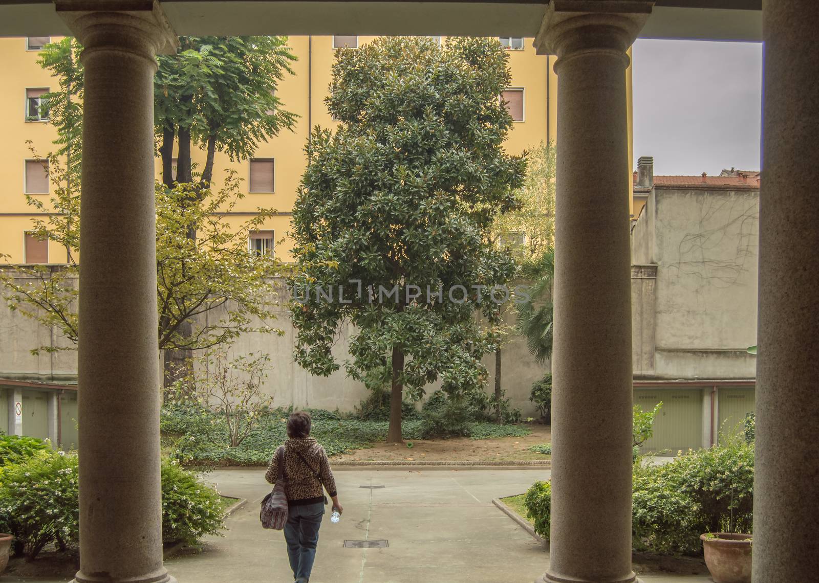 View of a female tourist from behind walking through the courtyard of an apartment building in Milan, Italy, early morning.