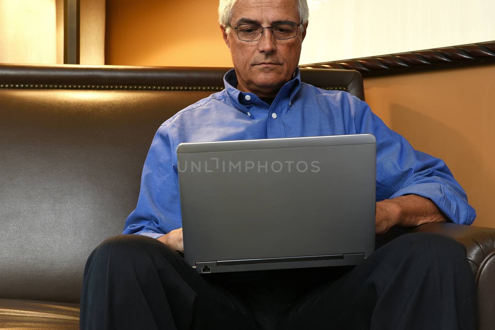 A senior businessman seated on a sofa in his hotel room and working on his laptop computer.