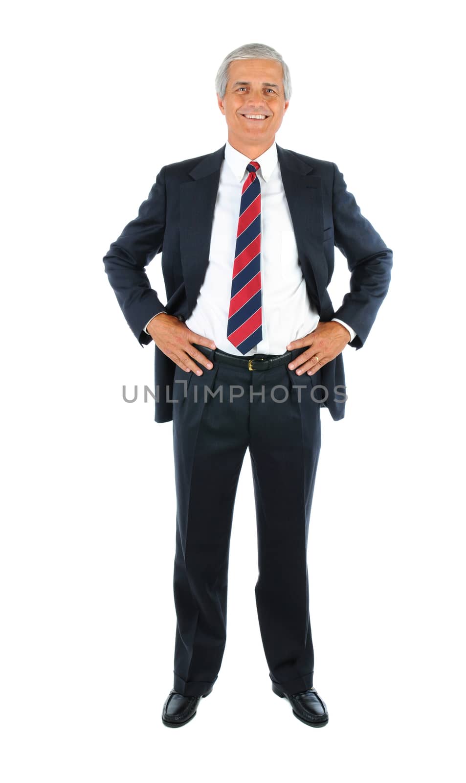 Smiling middle aged businessman in a suit and tie with his hands on hips. Full length over a white background.
